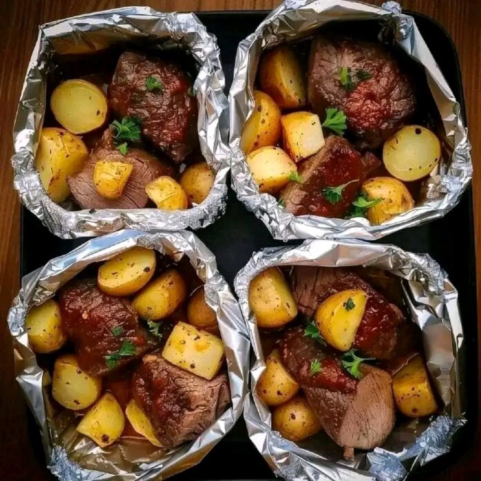 Four individual foil packets filled with garlic butter steak and potatoes on a dark tray. Each packet contains pieces of cooked steak, small potatoes, and chopped herbs.