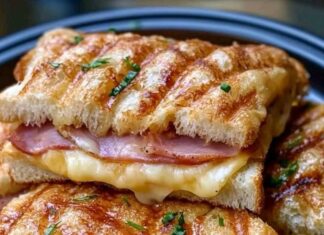 Hawaiian Ham and Cheese Sandwich Close-up of two halves of a grilled Hawaiian Ham and Cheese Sandwich stacked on a dark plate. The sandwich has grill marks and is filled with ham and melted cheese. Chopped herbs are sprinkled on top.