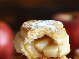 Apple Pie Biscuits A close-up shot of a stack of three apple pie biscuits on a white plate. The top biscuit is split open, revealing a filling of cooked apples. A red apple and a folded cloth are visible in the blurred background.