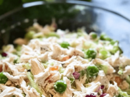 Deli-Style Chicken Salad A close-up shot of a clear glass bowl filled with deli-style chicken salad. The salad includes shredded chicken, mayonnaise, chopped celery, red onion, and green peas.