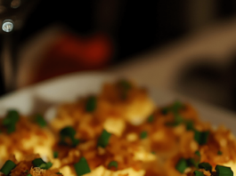 Deviled Eggs with Bacon and Cheddar A patterned plate filled with deviled eggs topped with crumbled bacon, shredded cheddar cheese, and chopped green onions.