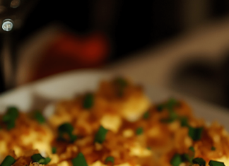 Deviled Eggs with Bacon and Cheddar A patterned plate filled with deviled eggs topped with crumbled bacon, shredded cheddar cheese, and chopped green onions.